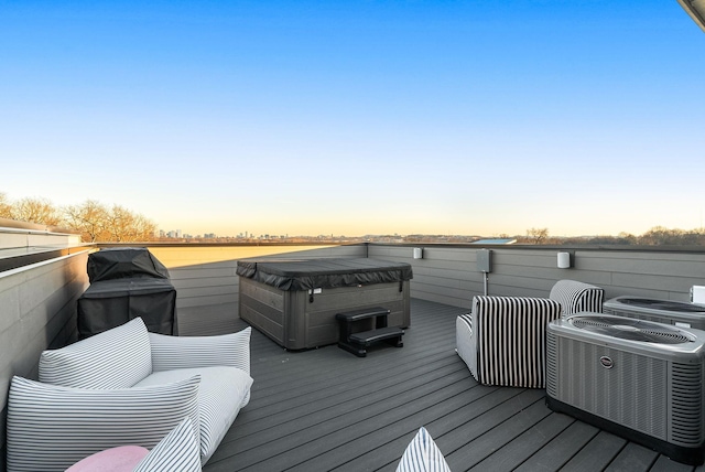 deck at dusk featuring a hot tub, a water view, and central AC