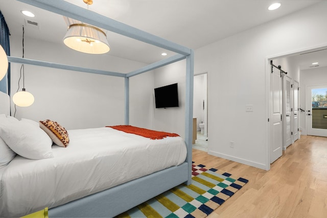 bedroom with ensuite bathroom, a barn door, and light hardwood / wood-style floors