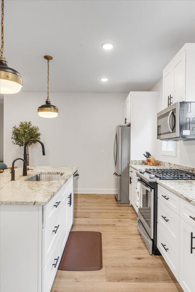 kitchen with appliances with stainless steel finishes, decorative light fixtures, sink, white cabinets, and light stone countertops