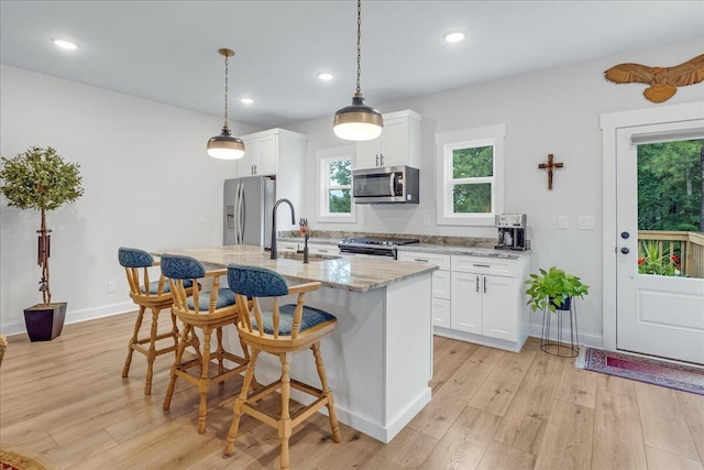 kitchen featuring light stone counters, stainless steel appliances, a center island with sink, and white cabinets