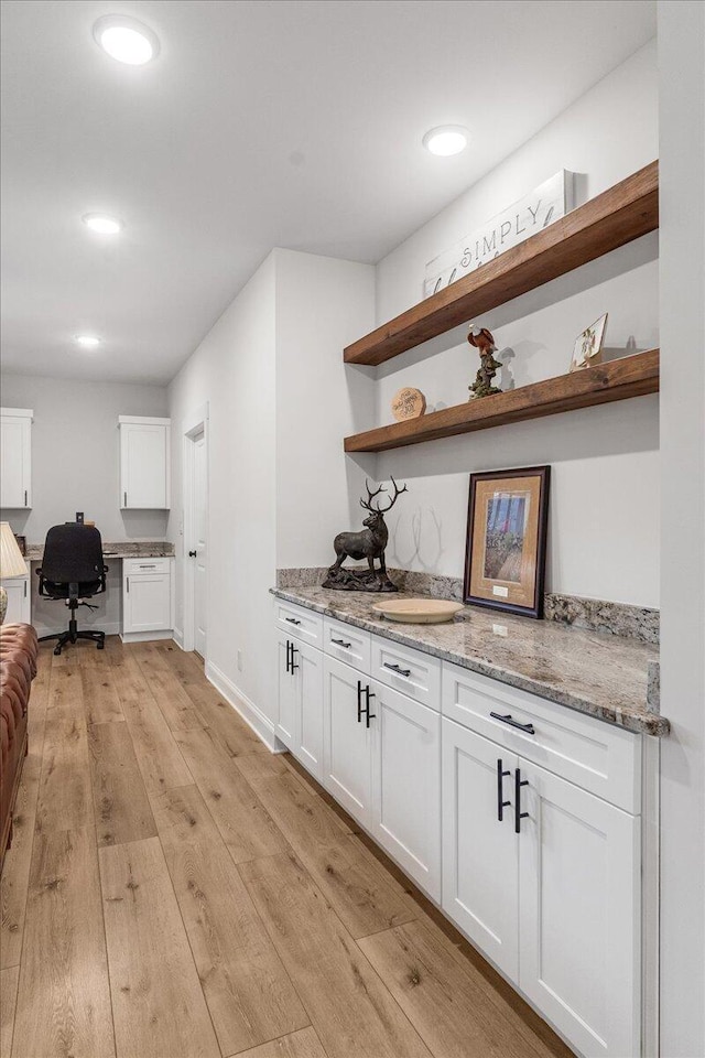 bar with white cabinetry, built in desk, light stone countertops, and light hardwood / wood-style flooring