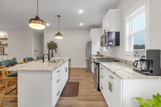 kitchen with a breakfast bar, sink, white cabinetry, appliances with stainless steel finishes, and pendant lighting