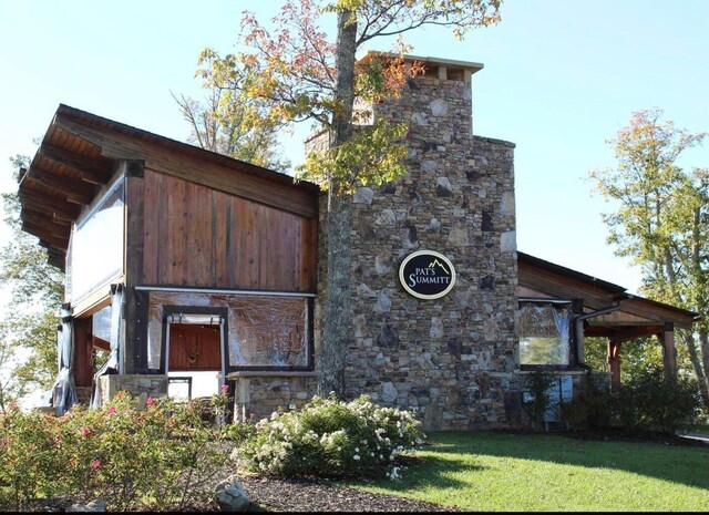 view of side of home with a chimney, a yard, and stone siding