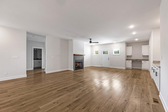 unfurnished living room featuring ceiling fan, visible vents, light wood-style floors, a warm lit fireplace, and recessed lighting