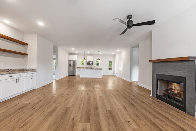 unfurnished living room featuring recessed lighting, a warm lit fireplace, a ceiling fan, light wood-style flooring, and baseboards