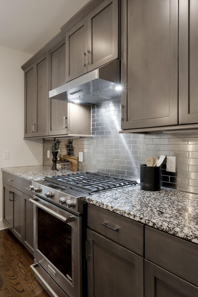 kitchen featuring gas range, decorative backsplash, ventilation hood, and light stone counters