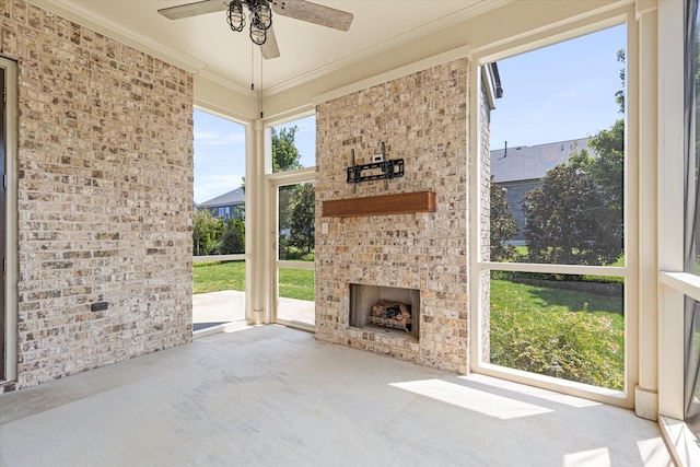 unfurnished living room with an outdoor brick fireplace, ornamental molding, ceiling fan, and brick wall