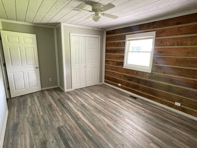 unfurnished bedroom with dark hardwood / wood-style floors, wood walls, ornamental molding, wood ceiling, and a closet