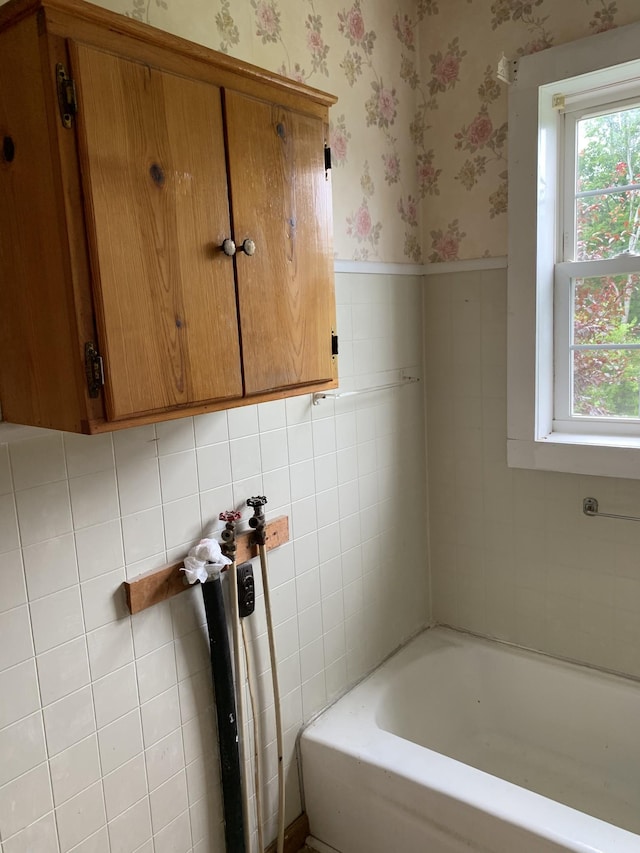 bathroom featuring tile walls, a bath, and a healthy amount of sunlight