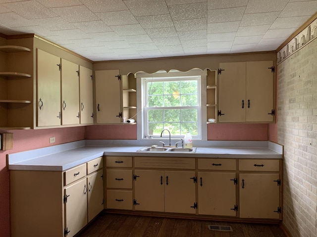 kitchen featuring brick wall, cream cabinets, sink, and dark hardwood / wood-style floors