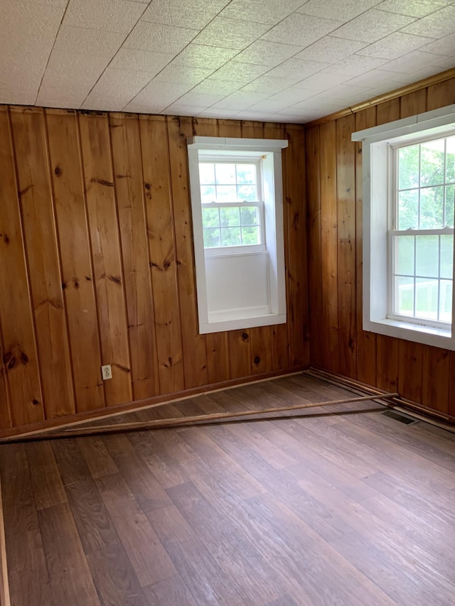 spare room with hardwood / wood-style flooring, wooden walls, and a healthy amount of sunlight