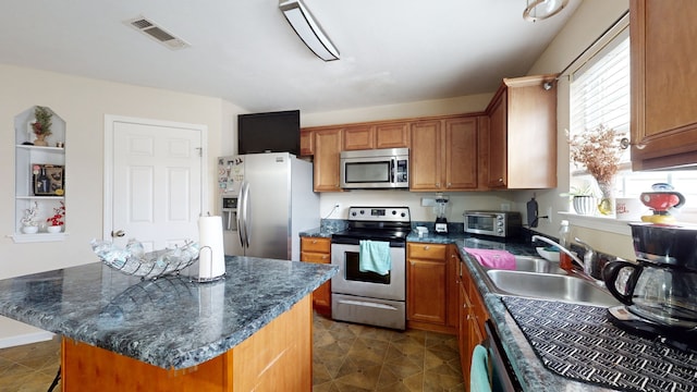 kitchen with appliances with stainless steel finishes, dark stone counters, sink, dark tile patterned flooring, and a center island