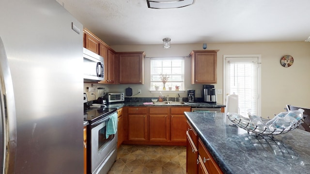 kitchen with appliances with stainless steel finishes, a wealth of natural light, tile patterned flooring, and sink