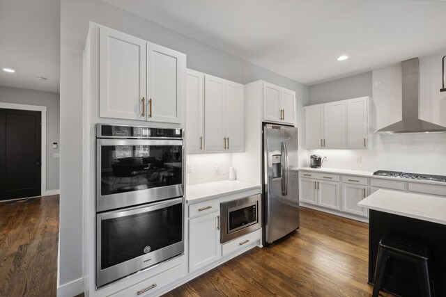 kitchen featuring stainless steel appliances, wall chimney range hood, white cabinets, and dark hardwood / wood-style flooring