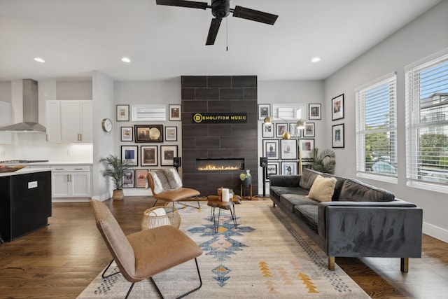 living room with a tiled fireplace, ceiling fan, and light hardwood / wood-style flooring