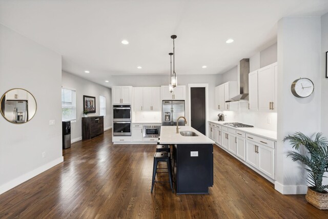 kitchen with wall chimney exhaust hood, sink, decorative light fixtures, a center island with sink, and stainless steel appliances