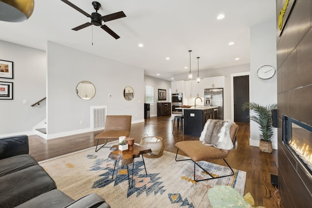 living room featuring ceiling fan, a fireplace, dark hardwood / wood-style floors, and sink