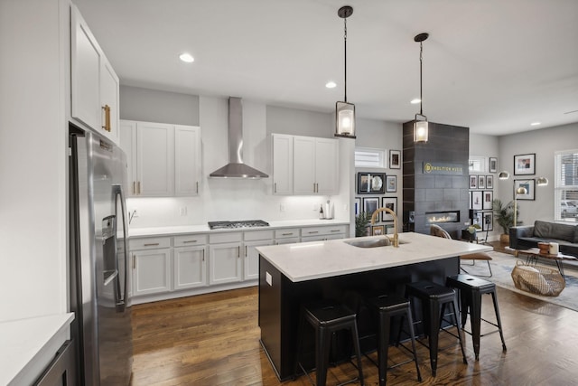 kitchen with sink, wall chimney range hood, a kitchen breakfast bar, stainless steel appliances, and white cabinets