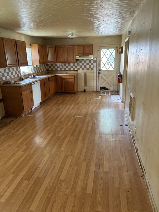 kitchen featuring sink, light hardwood / wood-style flooring, white dishwasher, tasteful backsplash, and a textured ceiling