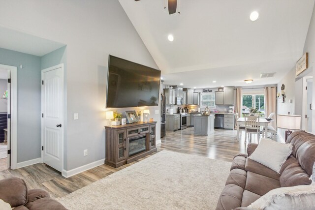 living room featuring light hardwood / wood-style flooring, high vaulted ceiling, and ceiling fan