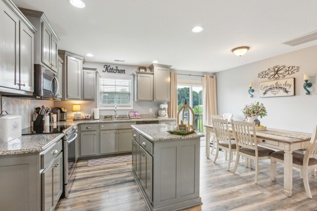 kitchen with light hardwood / wood-style floors, appliances with stainless steel finishes, light stone counters, and a healthy amount of sunlight