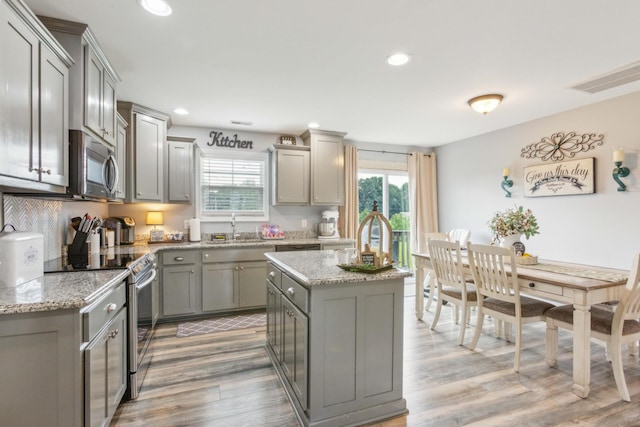 kitchen with light stone counters, gray cabinets, a kitchen island, stainless steel appliances, and light hardwood / wood-style floors