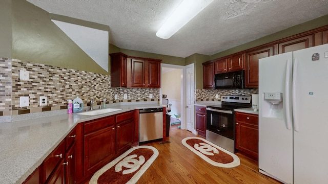 kitchen featuring sink, decorative backsplash, light hardwood / wood-style floors, stainless steel appliances, and a textured ceiling