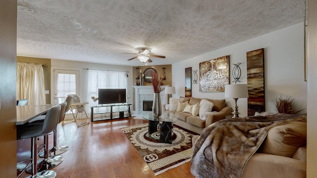 living room with hardwood / wood-style flooring, ceiling fan, a textured ceiling, and a fireplace