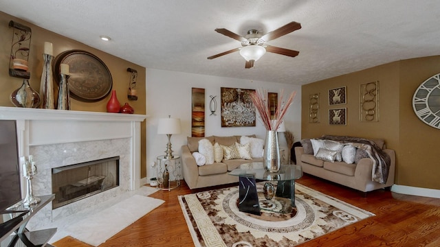 living room with dark wood-type flooring, ceiling fan, a high end fireplace, and a textured ceiling