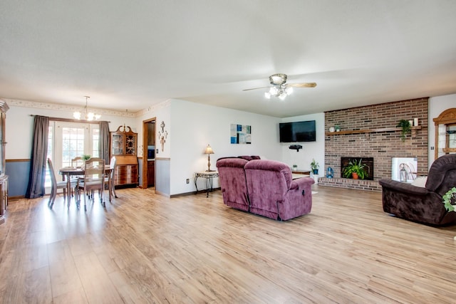 living room with ceiling fan with notable chandelier, light hardwood / wood-style floors, and a brick fireplace