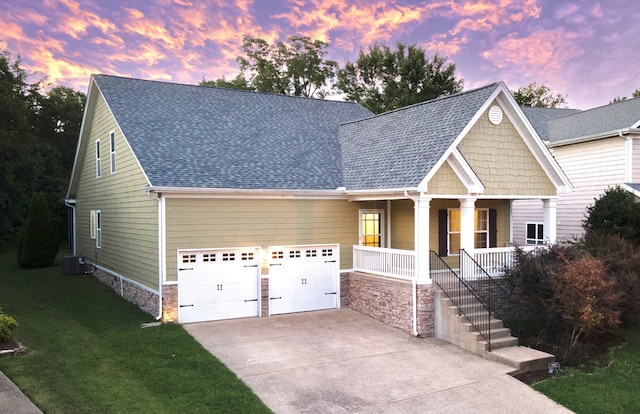 craftsman inspired home with driveway, a shingled roof, central AC unit, a porch, and a front yard