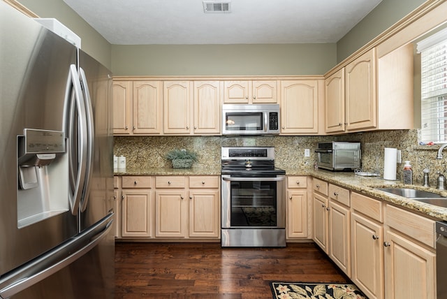 kitchen with light brown cabinets, light stone counters, dark hardwood / wood-style floors, appliances with stainless steel finishes, and backsplash