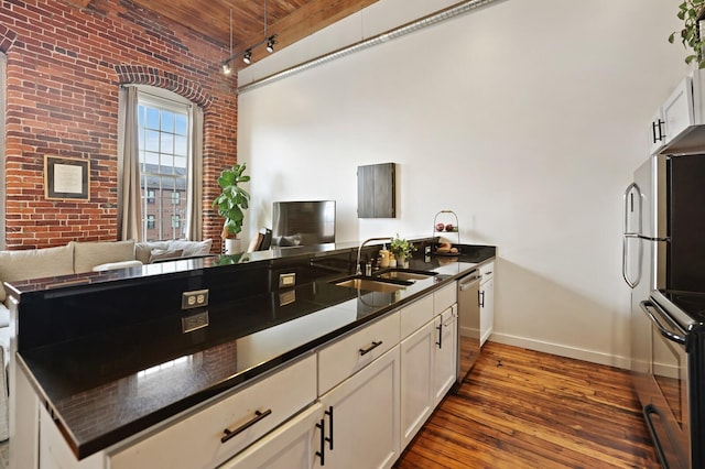 kitchen featuring track lighting, dishwasher, sink, brick wall, and hardwood / wood-style flooring