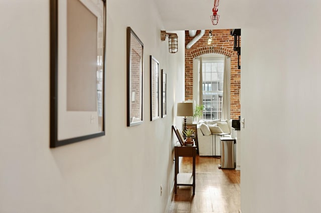 hall with light hardwood / wood-style flooring and brick wall