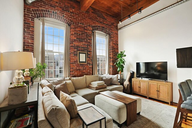 living room with track lighting, hardwood / wood-style floors, brick wall, wooden ceiling, and a towering ceiling