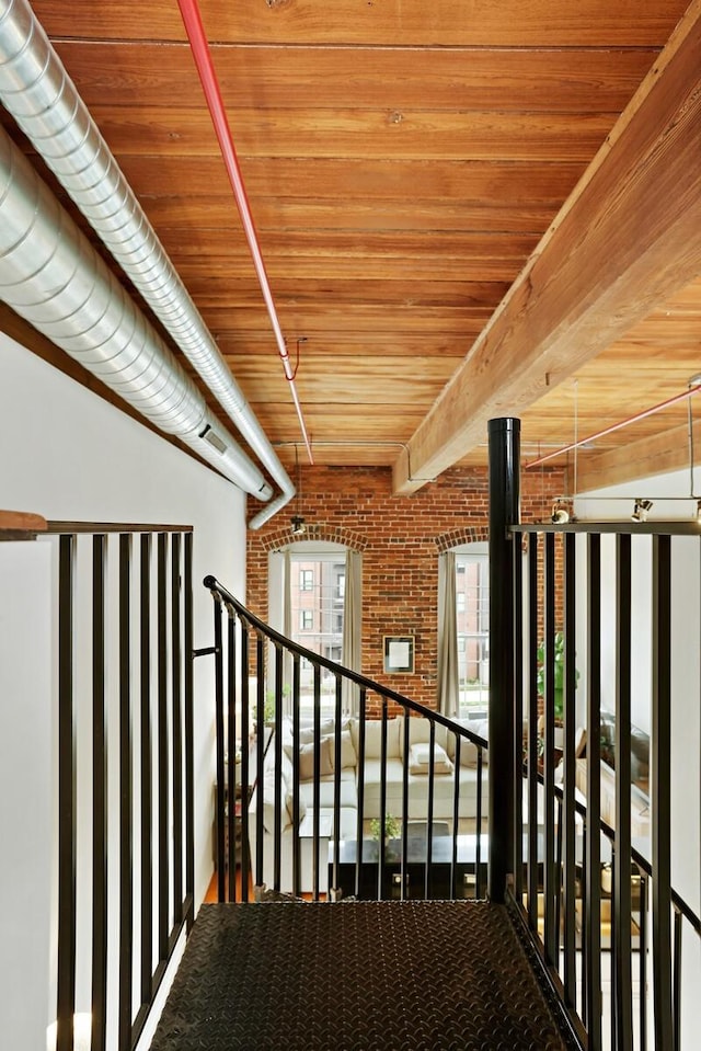 stairs with wood ceiling, brick wall, and beamed ceiling