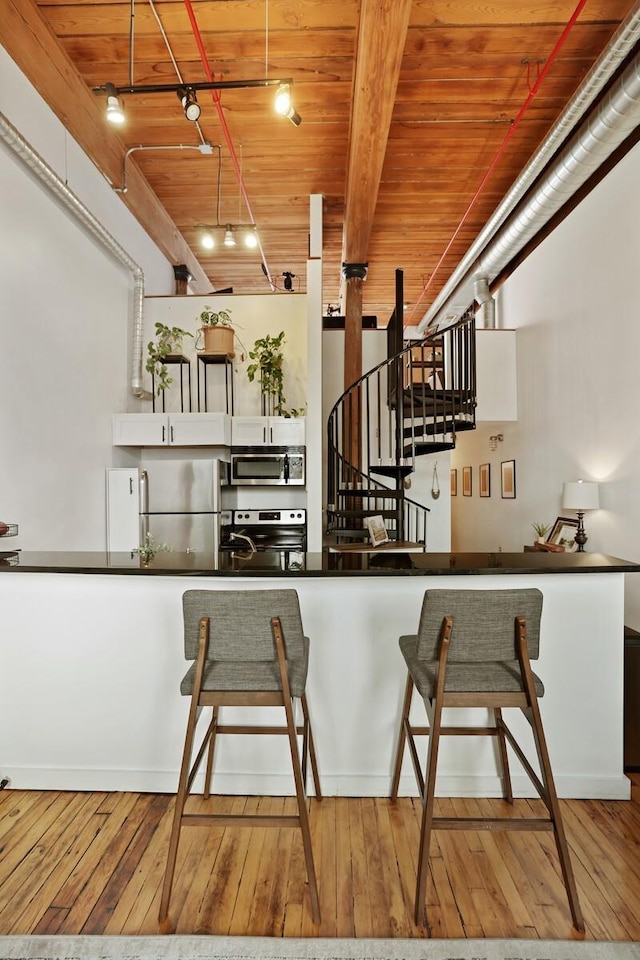 kitchen with appliances with stainless steel finishes, rail lighting, wood-type flooring, and wooden ceiling