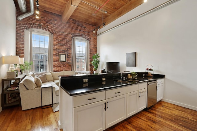 kitchen with sink, wood-type flooring, dishwasher, brick wall, and white cabinets