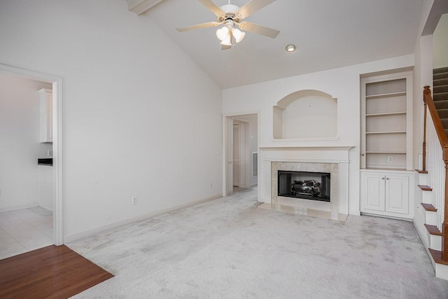 unfurnished living room featuring high vaulted ceiling, light colored carpet, ceiling fan, a high end fireplace, and built in shelves