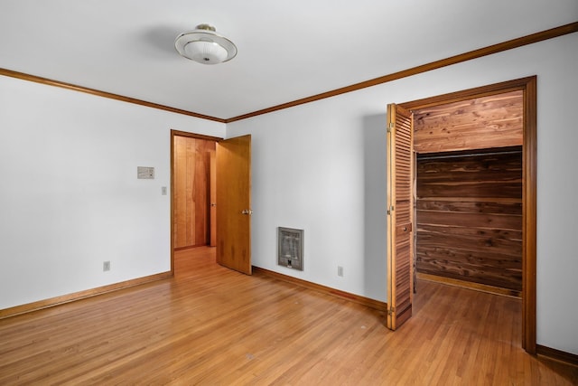 unfurnished bedroom with heating unit, light wood-style floors, baseboards, and crown molding