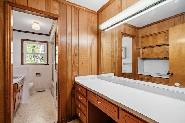 bathroom with toilet, crown molding, vanity, wood walls, and tile walls