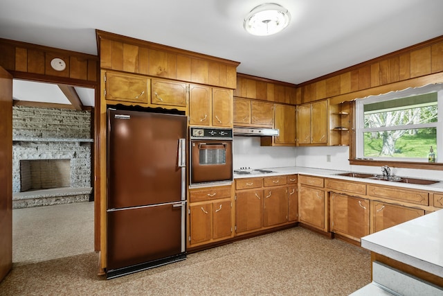 kitchen featuring a stone fireplace, sink, black oven, and fridge