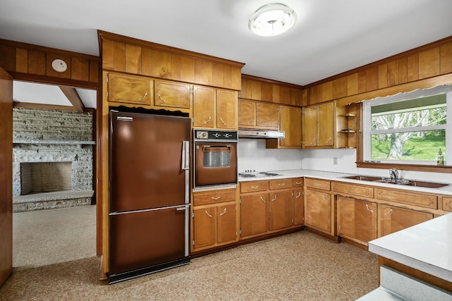 kitchen with wall oven, brown cabinets, refrigerator, light countertops, and a sink