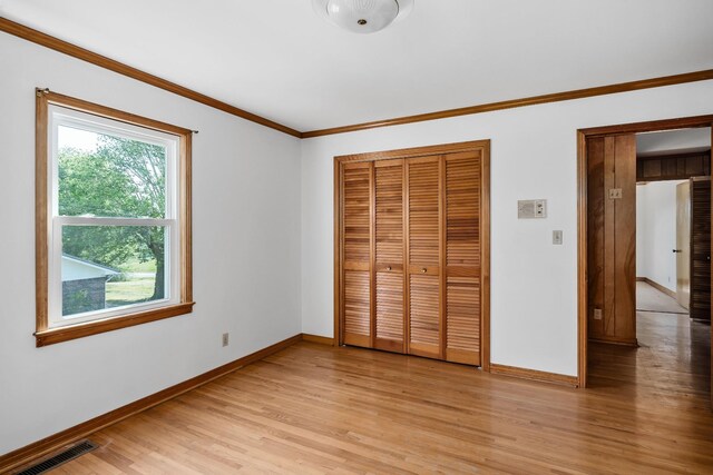 unfurnished bedroom with crown molding, light wood-type flooring, and a closet