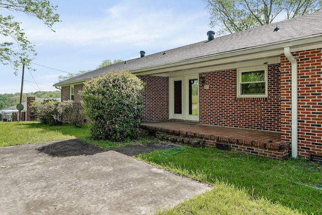 rear view of property with a yard, brick siding, roof with shingles, and a patio area