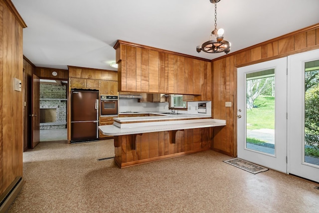 kitchen featuring oven, a peninsula, light countertops, fridge, and brown cabinets