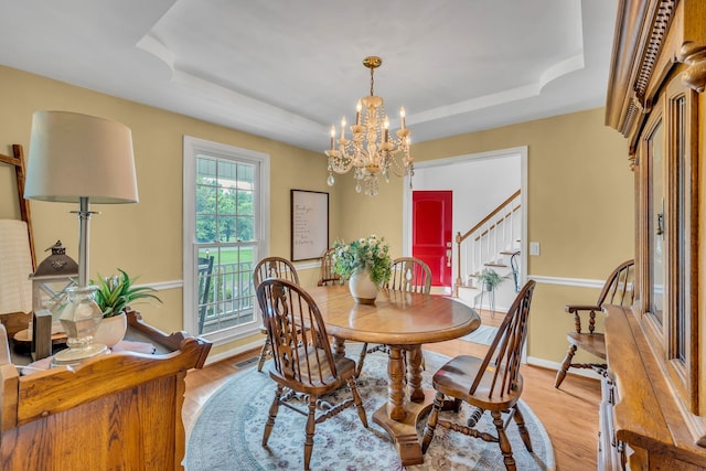 dining area featuring a raised ceiling, an inviting chandelier, and light wood-type flooring