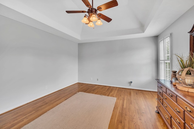 spare room with ceiling fan, light wood-type flooring, and a raised ceiling