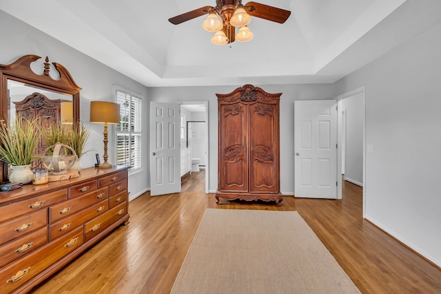 bedroom featuring ensuite bath, light hardwood / wood-style floors, and a tray ceiling