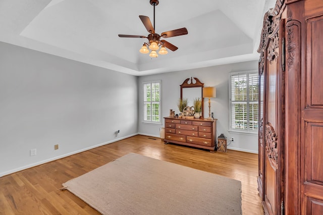 bedroom featuring light hardwood / wood-style floors, ceiling fan, and a tray ceiling